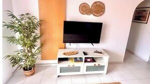 Un salon équipé d’un téléviseur à écran plat, d’une plante en pot, d’un meuble en bois et d’un élément décoratif mural.