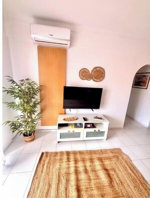 A living room with a flat-screen TV, a potted plant, a wooden cabinet, and a decorative wall piece. - Beach Front + Castle and sea view Home in Heart of Ferragudo (Ferragudo)