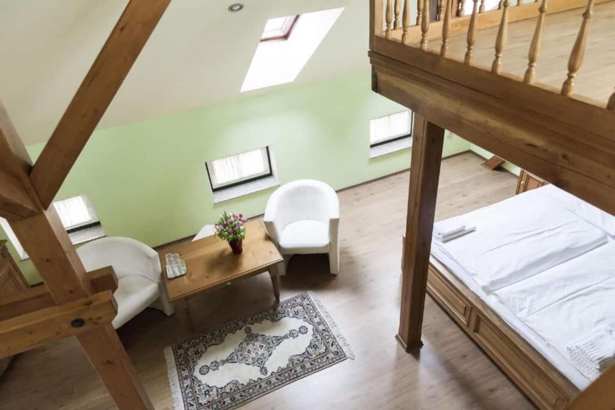 A loft-style room with a wooden bed, a white chair, a small table with a plant, and a patterned rug.