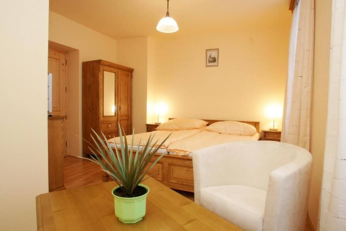A bedroom with a bed, bedside tables, a chair, a wooden wardrobe, and a potted plant.