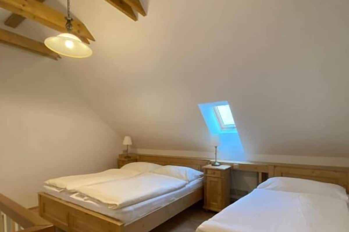 A room with two wooden beds, a small table, a lamp, and a skylight.