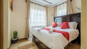 A hotel room with a bed, curtains, a potted plant, and a ceiling light. - Kivulini luxurious and cozy apartment (Thika)