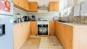 A compact kitchen with wooden cabinets, a refrigerator, a stove, and a coffee maker. - Kivulini luxurious and cozy apartment (Thika)