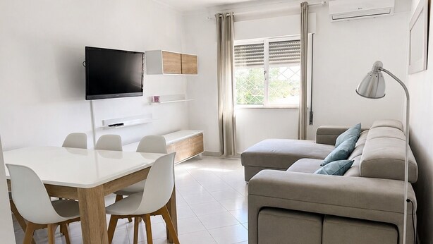 Un saló modern amb televisió de pantalla plana, un sofà, una taula de dinar amb cadires i una finestra amb cortines.