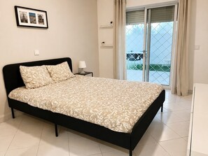 Ein Schlafzimmer mit einem Bett, einem Nachttisch, einem gerahmten Bild und einer Glasschiebetür zu einem Außenbereich.