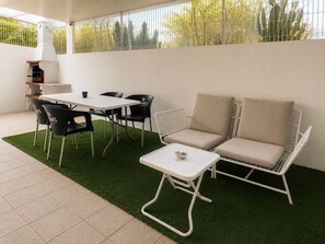 Eine Terrasse mit einem weißen Tisch, schwarzen Stühlen, einem beigen Sofa und einem kleinen weißen Tisch mit einer Muschel.