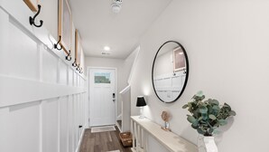 Un couloir avec une porte blanche, un miroir, une lampe et une plante posée sur une console.
