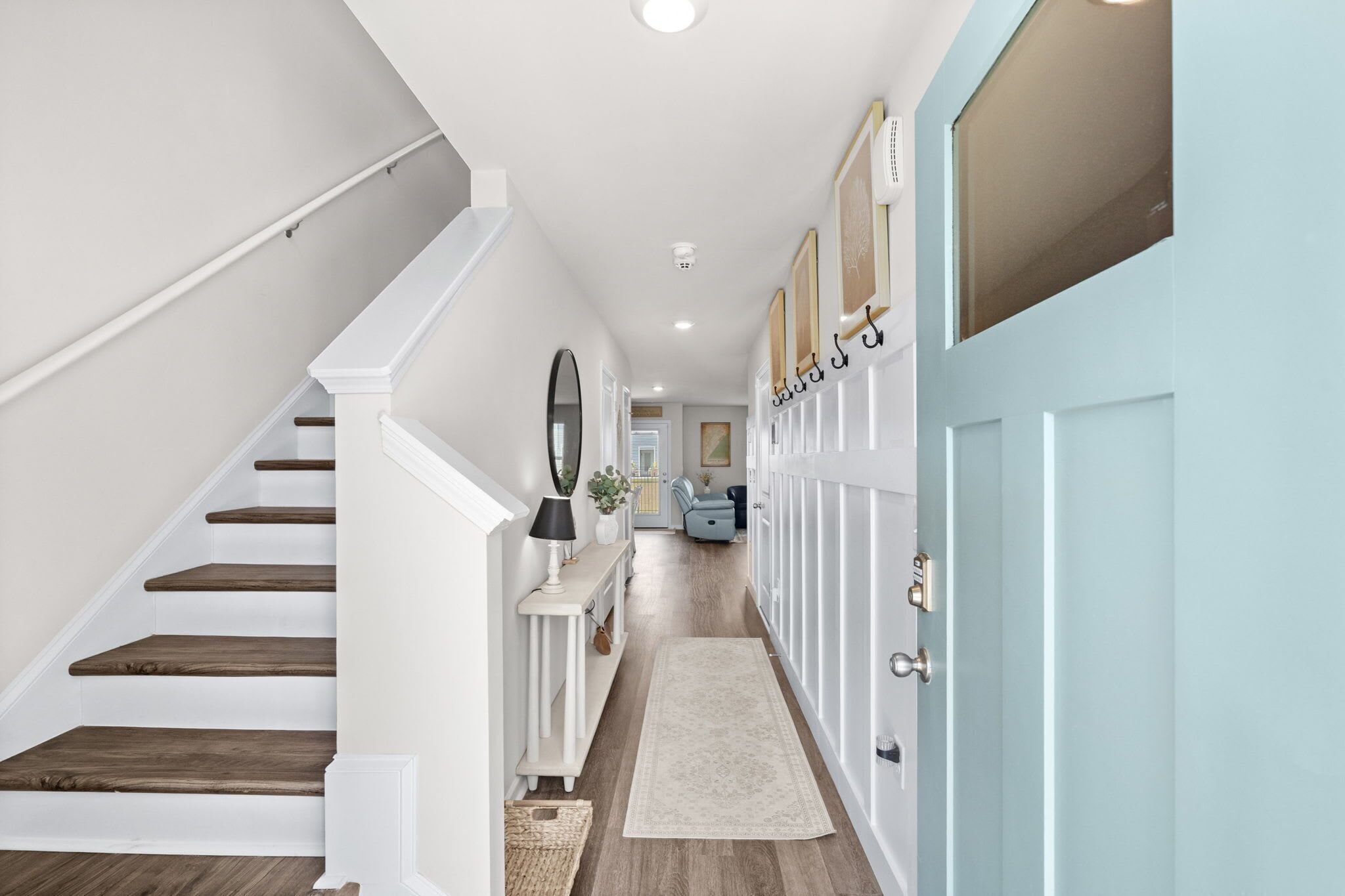 A hallway with a staircase, a console table with a lamp, a mirror, and a door with a lock.