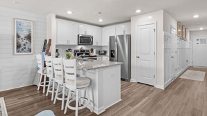 Une cuisine moderne avec des meubles blancs, des appareils en acier inoxydable et un coin bar doté de tabourets blancs.