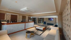 Vestíbulo de hotel con mostrador de recepción, zona de estar y una pantalla de televisión.