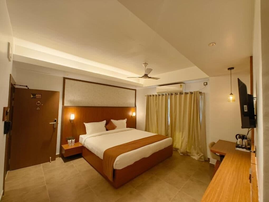 A hotel room with a bed, a desk, a TV, a ceiling fan, and a door.