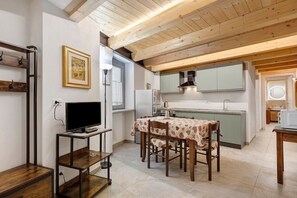 A compact kitchen with a dining table, wooden beams, and a framed picture on the wall. - Apartment '3' with Private Parking, Shared Garden, Central Morgex Location (Morgex)