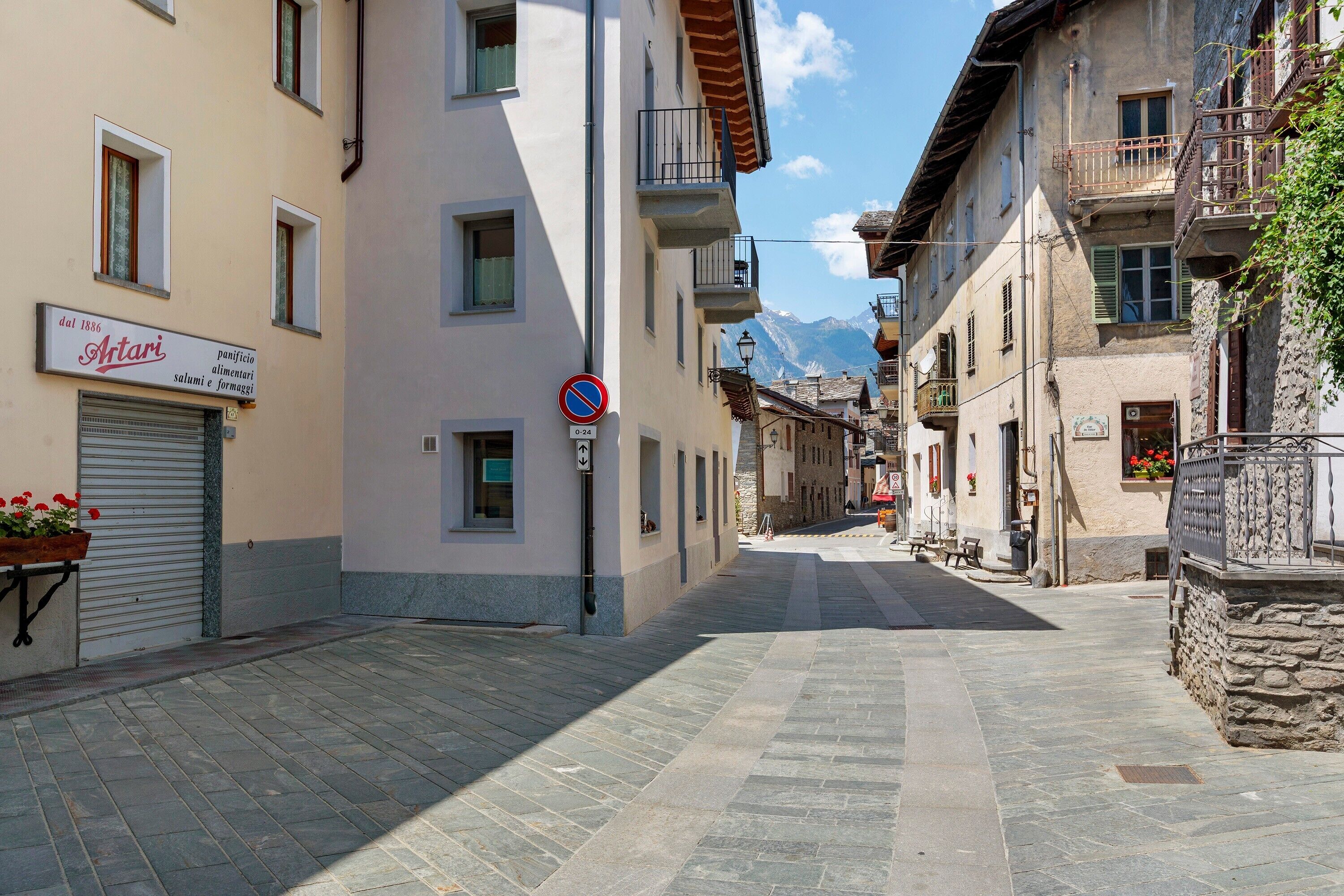 Una calle estrecha flanqueada por edificios, un cartel de 'prohibido estacionar' y una tienda llamada 'Antari' con un letrero que indica que abrió en 1886.