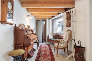 A cozy living room with a grand piano, a patterned rug, a wooden bench, a sofa with floral upholstery, and a wall-mounted clock.