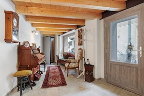 A room with a piano, a wooden chair, a red rug, a wooden door, and a window.