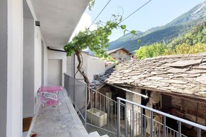 Un balcon doté d’un toit en pierre, d’une rambarde en métal et offrant une vue sur un paysage montagneux.
