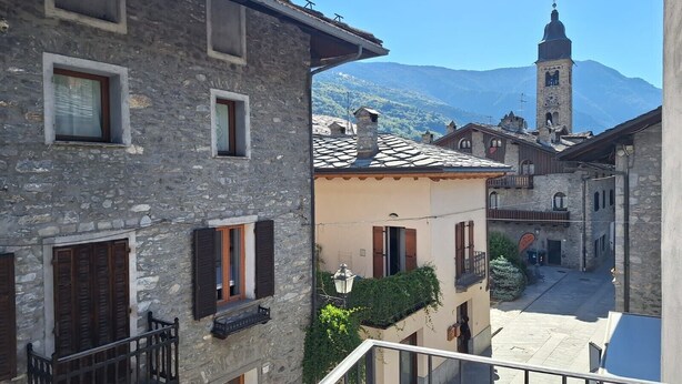A stone building with a balcony, a clock tower in the background, and a mountain view. - Studio with Private Parking, Shared Garden, and Walk-in Closet (Morgex)