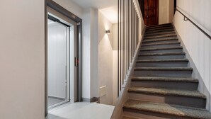 A staircase with a handrail, a door with a sliding glass panel, and a wall-mounted light fixture. - Studio with Private Parking, Shared Garden, and Walk-in Closet (Morgex)