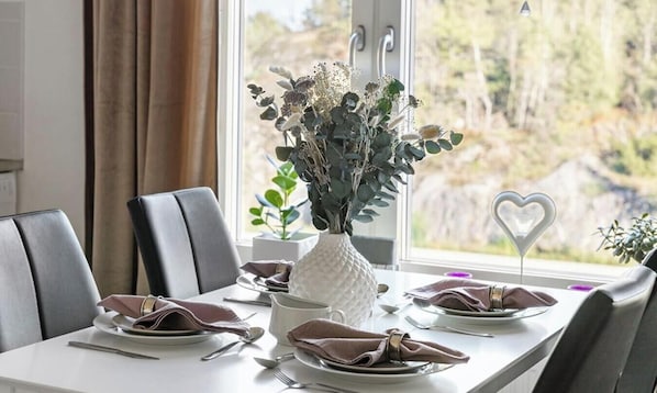 Une table à manger dressée avec des assiettes, des couverts et un vase rempli de fleurs.