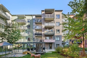 Um edifício residencial com vários andares, varandas, uma área de estar coberta ao ar livre e um pequeno jardim.