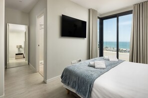 Ein Hotelzimmer mit Bett, Fernseher, Meerblick und einem Badezimmer mit Spiegel und Handtuchhalter.