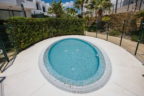 Ein Schwimmbecken mit gefliestem Rand, umgeben von einem Zaun und einem Heckenstreifen.