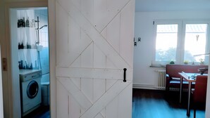 Ein Zimmer mit weißer Tür, einer Waschmaschine, einem Heizkörper, einem Fenster mit Blick und einem Tisch mit Stühlen.