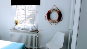 Ein Zimmer mit einem weißen Heizkörper, einem weißen Stuhl, einem kleinen Tisch mit einer Pflanze, einem dekorativen Gegenstand und einem Fenster mit Jalousien.