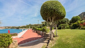 A coastal walkway with a red path, a well-maintained hedge, and a view of the sea. - GuestHost - Porto Cervo Spacious Flat by the Port (Arzachena)