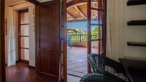 A room with a wooden door leading to a balcony with a view of buildings and greenery. - GuestHost - Porto Cervo Spacious Flat by the Port (Arzachena)