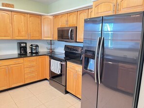 Eine Küche mit Holzschränken, einem Edelstahlkühlschrank, einer Mikrowelle, einem Backofen und einer Kaffeemaschine.