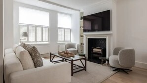 A living room with a sofa, a coffee table, a fireplace, and a TV mounted on the wall. - Chelsea White House Retreat 3 Bedroom House (London)