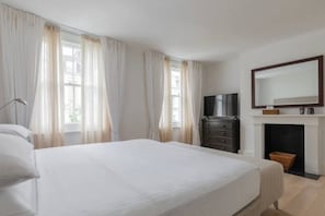 A bedroom with a bed, a dresser, a television, and a fireplace. - Chelsea White House Retreat 3 Bedroom House (London)