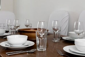 A dining table set with white plates, bowls, and clear glasses, with a wooden bowl centerpiece. - Chelsea White House Retreat 3 Bedroom House (London)