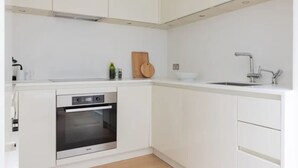 A modern kitchen with white cabinetry, a built-in oven, a wooden cutting board, and a stainless steel sink. - Chelsea White House Retreat 3 Bedroom House (London)