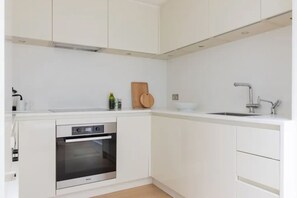 A modern kitchen with white cabinetry, a built-in oven, a wooden cutting board, and a stainless steel sink. - Chelsea White House Retreat 3 Bedroom House (London)