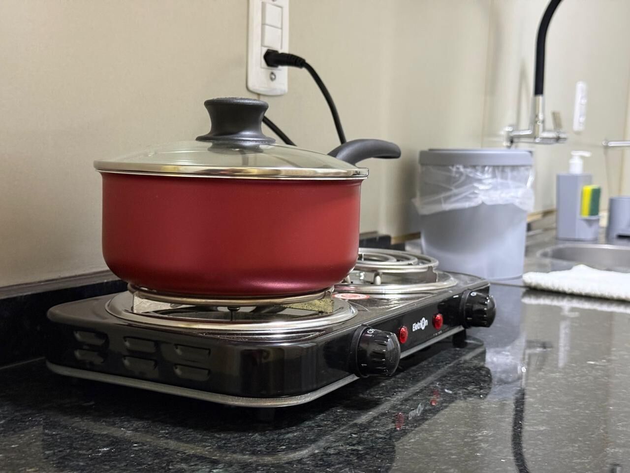 A red pot on a portable gas stove with a power cord plugged in.