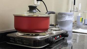 A red pot on a portable gas stove with a power cord plugged in.