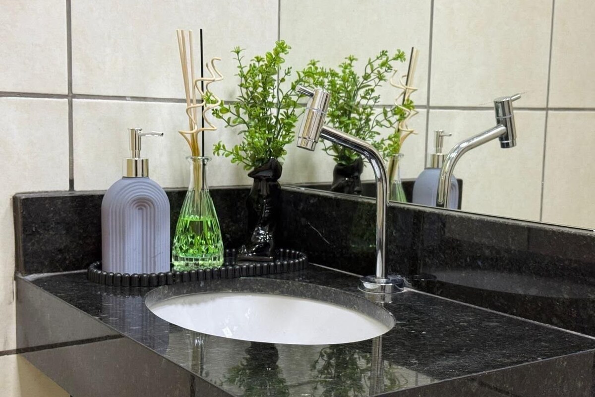A bathroom sink with a modern faucet, a soap dispenser, and a glass container with a plant.