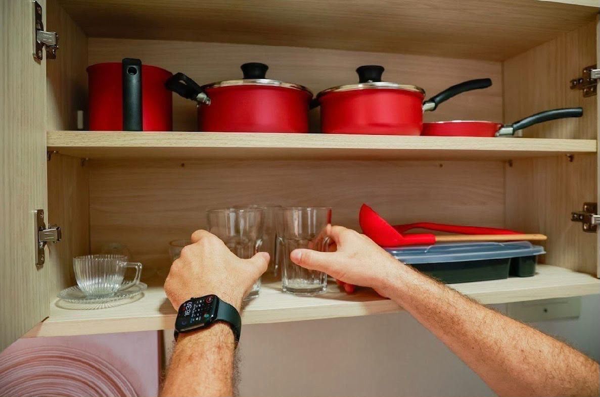 Un armario de cocina con ollas y sartenes rojas, un juego de vasos y un utensilio con mango rojo.