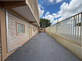 Um edifício com fachada de tijolos, galeria coberta e cerca de metal.