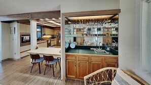 A modern kitchen with wooden cabinets, a dining area with chairs, and a built-in glass display for kitchenware. - Akvavit | Oceanfront w/Game Room + Direct Beach Access (Ponte Vedra)