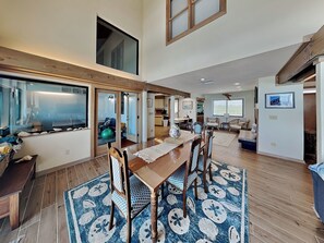 A spacious living area with a dining table, chairs, and a large window. - Akvavit | Oceanfront w/Game Room + Direct Beach Access (Ponte Vedra)