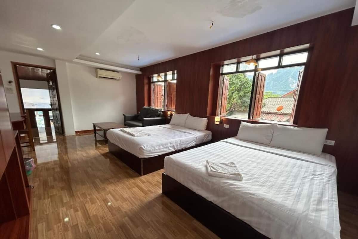 Habitación de hotel con dos camas, piso de madera, un escritorio y ventanas amplias con vistas.