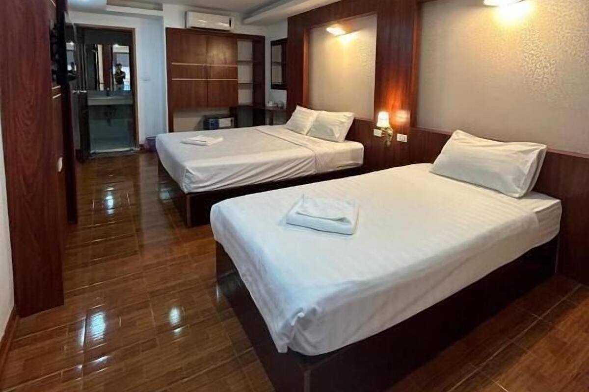 Habitación de hotel con dos camas, suelo de madera, un armario y un espejo.