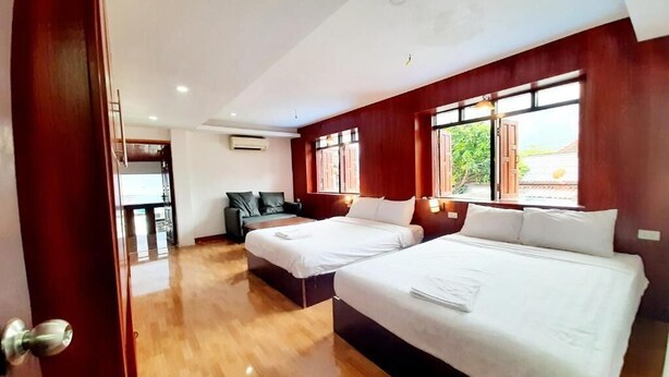 Habitación de hotel con dos camas, suelo de madera y ventanas amplias.