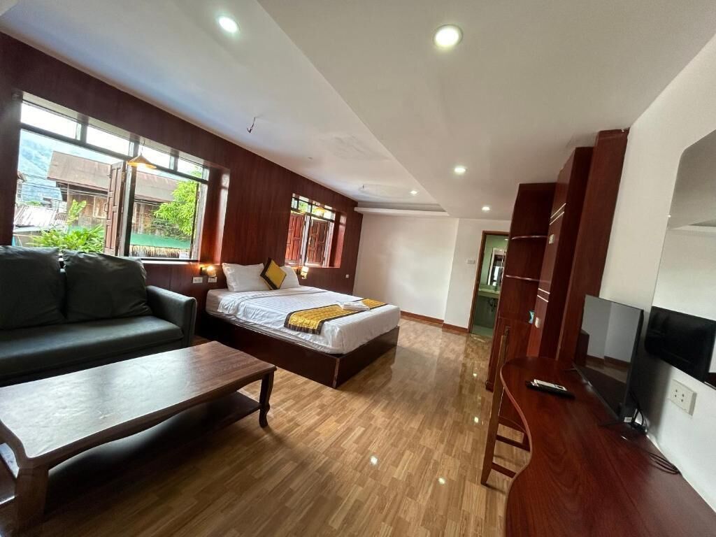 Ein Hotelzimmer mit Bett, einer Couch, einem Couchtisch, einem Fernseher und einem Fenster mit Blick ins Grüne.