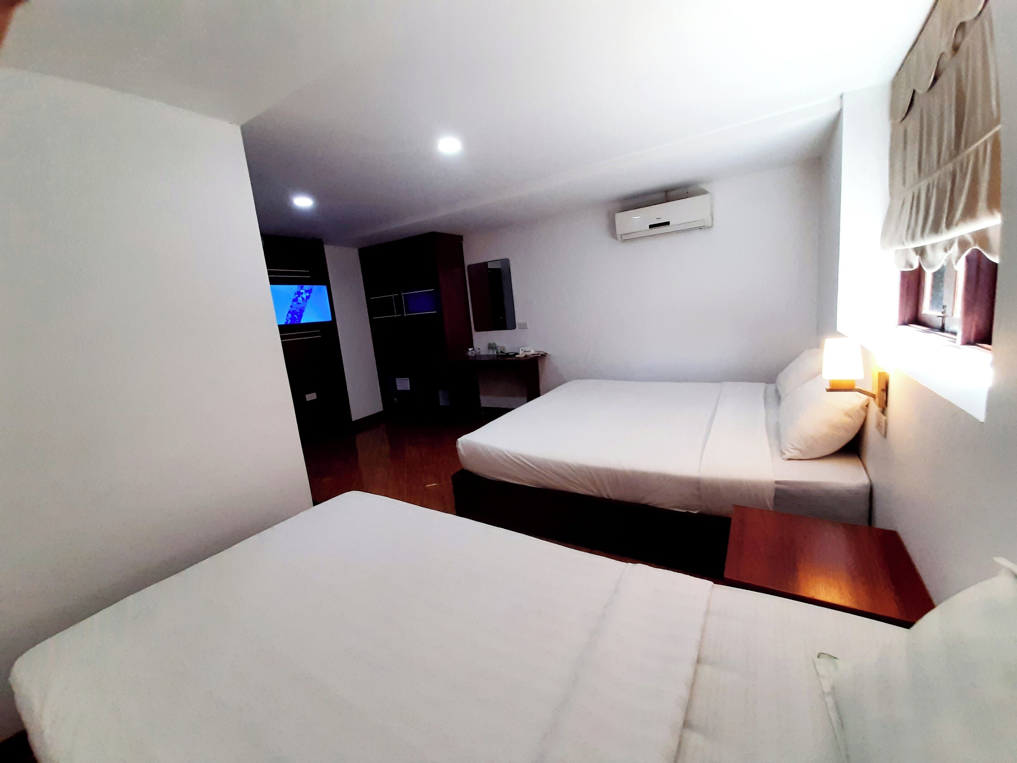 A small, clean room with two beds, a TV, and a window with curtains.