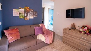 Ein Wohnzimmer mit einer Couch, einem Fernseher und einer Holzkombination mit Schubladen.