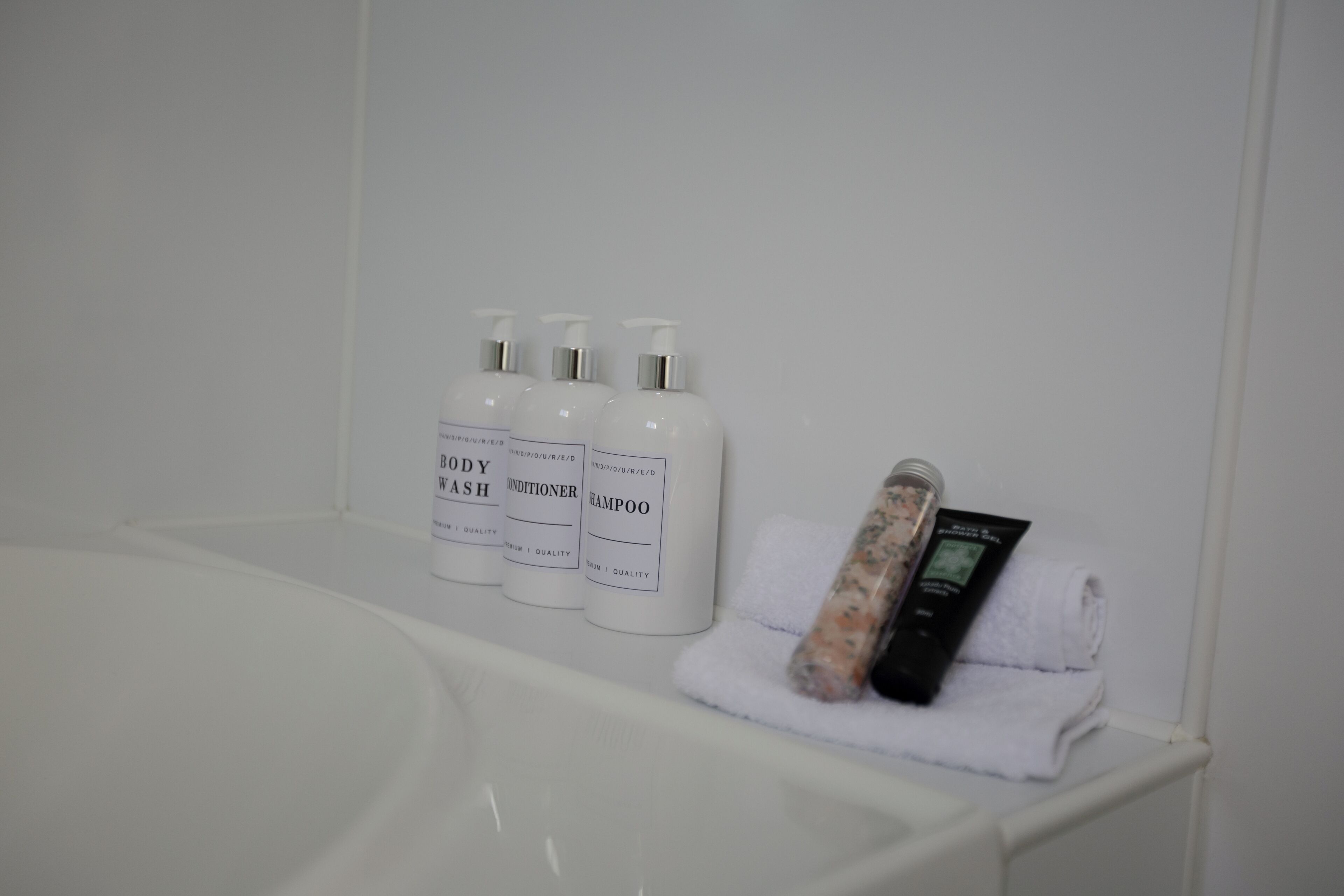 A bathroom with a white bathtub, three bottles of body wash, conditioner, and shampoo, and a bar of soap.